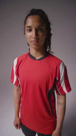 Vertical-Video-Studio-Shot-Of-Female-Footballer-Wearing-Club-Kit-Against-Grey-Background-Catching-Ball